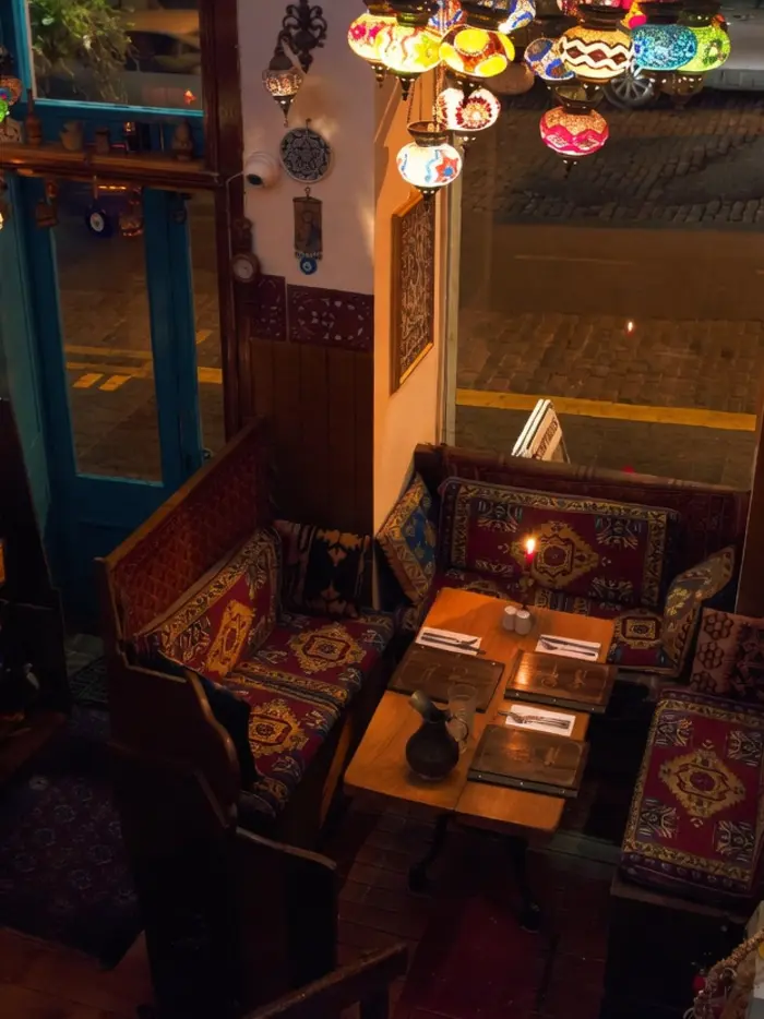 Dining nook with kilim-covered benches under dozens of mosaic lamps